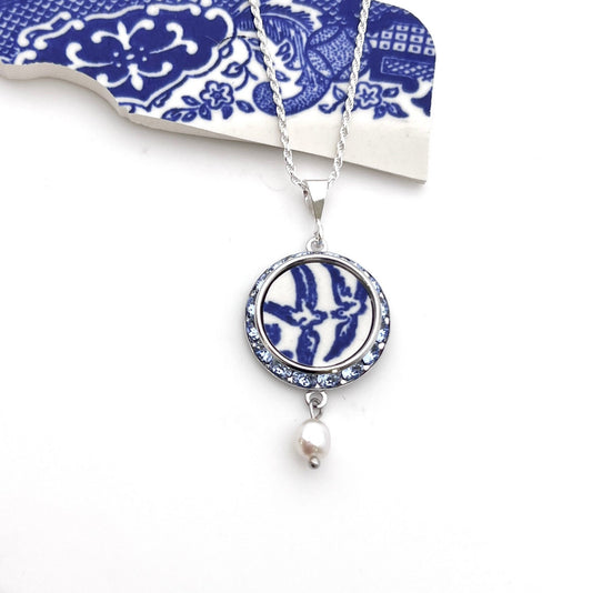 Necklace with a handmade round pendant that features love birds on a vintage blue willow china pattern. Sparkly crystals surround the china in a silver-tone frame. Pendant is 1 inch round with a sterling silver chain, loop style bail and pearl drop.
