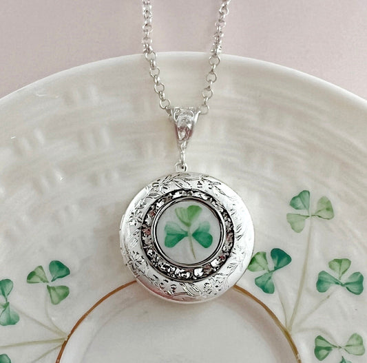 May include: Silver locket necklace with a shamrock design. The locket features a detailed silver filigree frame and a circular, clear glass insert showcasing a green shamrock. The necklace has a delicate silver chain. This Irish-themed pendant is perfect for St. Patrick&#39;s Day or any occasion.
