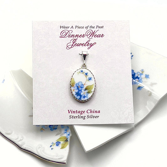 May include: A silver oval pendant with a vintage china cameo featuring blue flowers on a white background. The pendant is on a white card with the text &#39;Wear A Piece of the Past Dinner Wear Jewelry&#39; and &#39;Vintage China Sterling Silver&#39;.