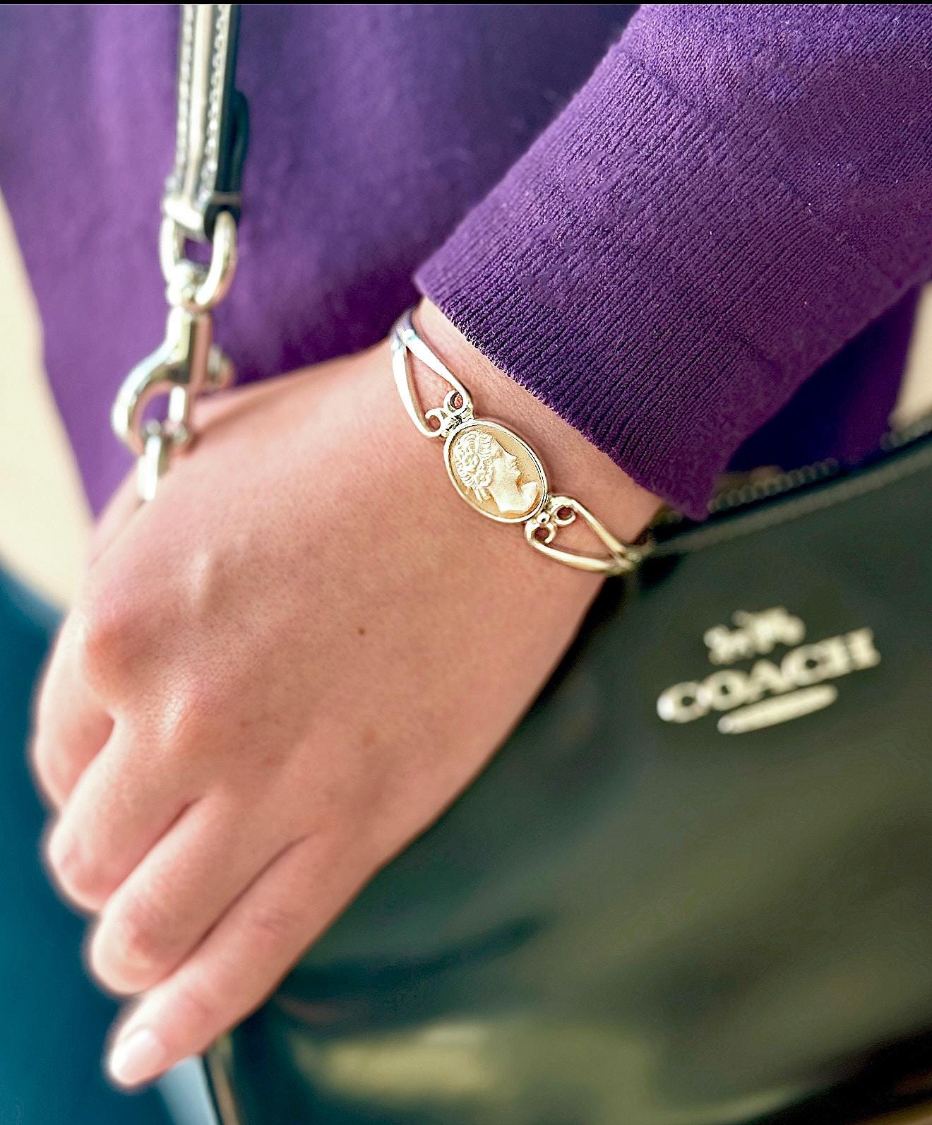 May include: A silver bracelet with a cameo featuring a woman's profile. The cameo is set in an oval shape and is surrounded by a delicate silver design.