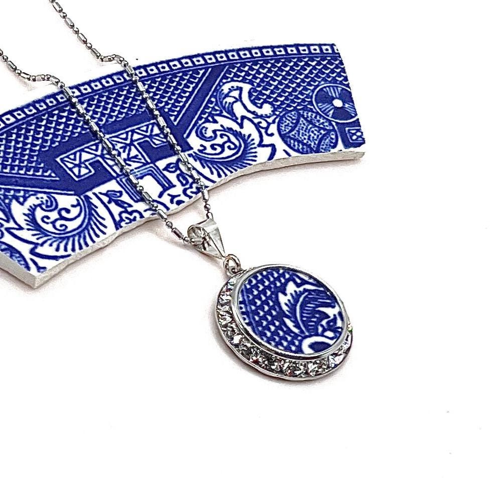 May include: A silver chain necklace with a blue and white porcelain pendant. The pendant is surrounded by clear rhinestones.