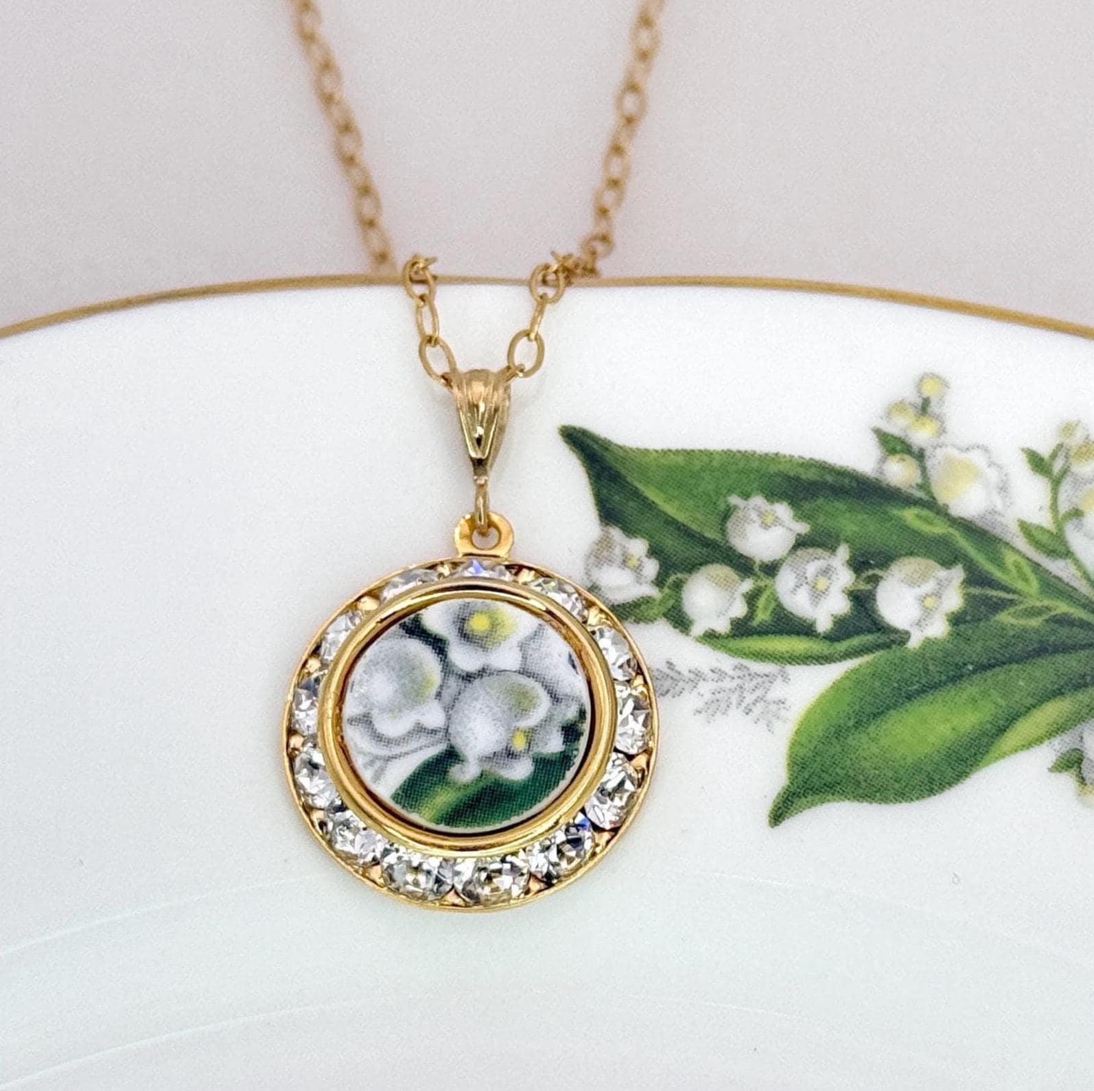 May include: A gold-toned necklace with a round pendant featuring a floral design. The pendant is encircled by a row of clear crystals. The necklace hangs on a delicate chain, showcasing a vintage-inspired aesthetic.